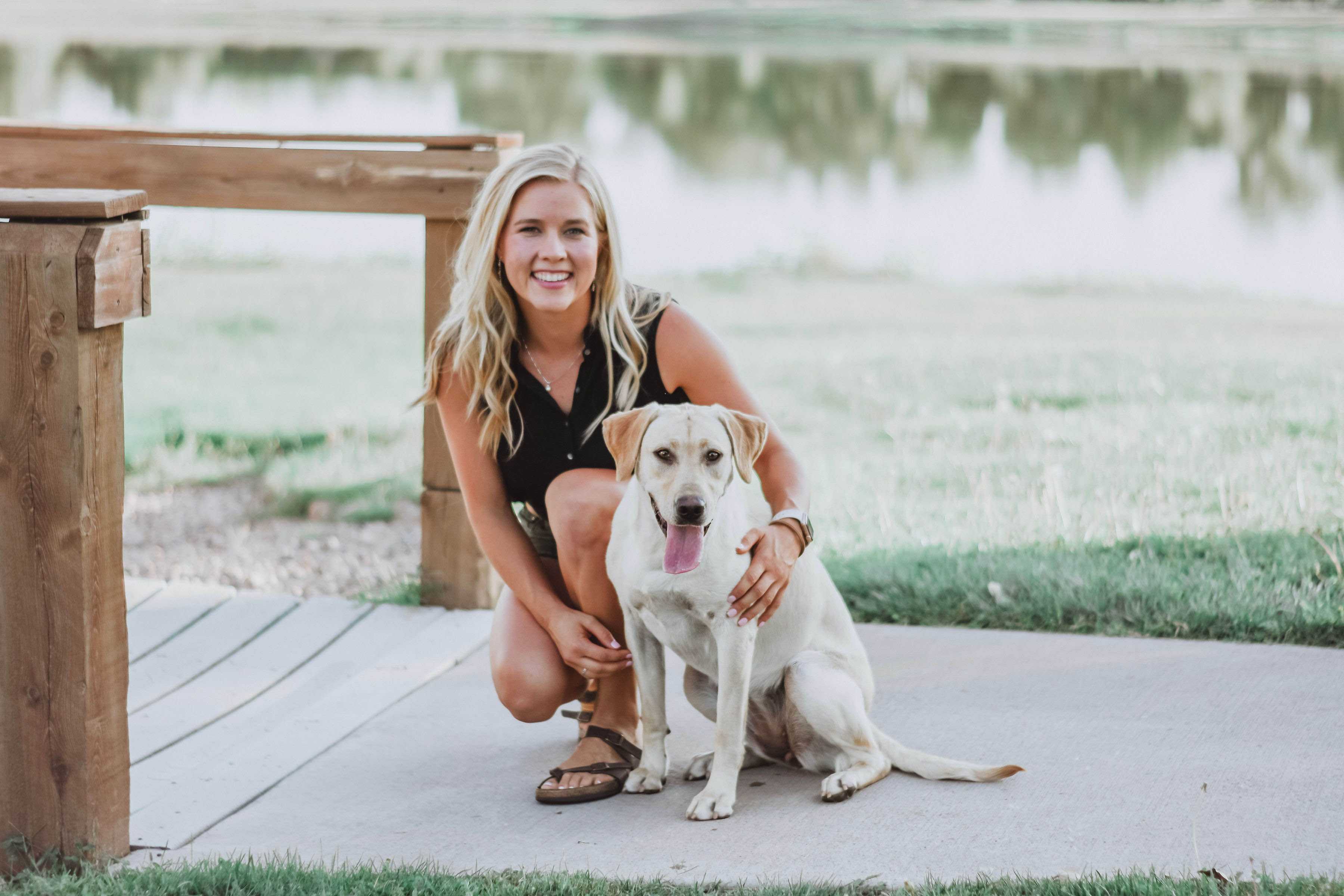Trainer kneeling beside a yellow lab near a lake